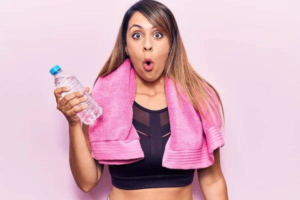 Young beautiful woman wearing sportswear and towel holding bottle of water scared and amazed with open mouth for surprise, disbelief face