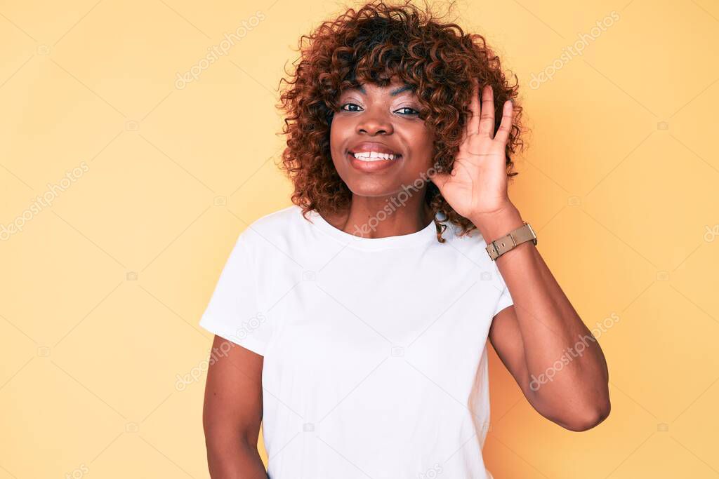 Young african american woman wearing casual white t shirt smiling with hand over ear listening and hearing to rumor or gossip. deafness concept. 