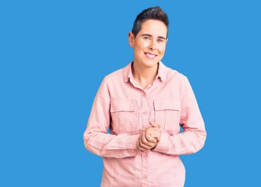 Kısa saçlı, sıradan kıyafetler giyen, elleri çapraz parmaklı, gevşemiş ve neşeli gülümseyen genç bir kadın. Başarı ve iyimserlik 