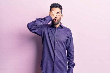 Sakallı, sıradan bir gömlek giyen, yüzü ve gözleri kapalı, utangaç bir ifadeyle parmaklarının arasından bakan genç ve yakışıklı bir adam.. 