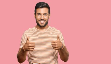 Yakışıklı İspanyol bir adam günlük kıyafetler giyiyor. Başarı işareti yapıyor. Elleriyle olumlu jest yapıyor. Neşeli ifade ve kazanan jest. 