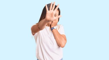 Güzel, beyaz tişört giyen beyaz bir kadın elleriyle gözlerini kapatıyor ve üzgün ve korku ifadeleriyle jestleri durduruyor. utangaç ve olumsuz kavram. 