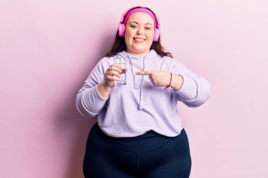 Genç ve cüsseli bir kadın bir bardak su içiyor. Kulaklık takıyor, gülümsüyor. 