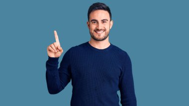 Gündelik kıyafetler giyen genç yakışıklı bir numarayı gösterip işaret ederken kendinden emin ve mutlu bir şekilde gülümsüyor.. 
