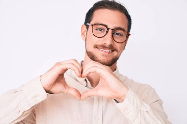 Gündelik kıyafetler ve gözlük takan genç yakışıklı bir adam. Aşkla gülümsüyor. Kalp sembolü ve elleri ile şekil veriyor. romantik kavram. 