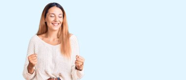 Güzel, genç bir kadın gündelik kıyafetler giyip çok mutlu ve heyecanlı bir şekilde kollarını kaldırıp, gülümseyerek ve başarı için çığlık atarak kazanan bir jest yapıyor. kutlama konsepti. 