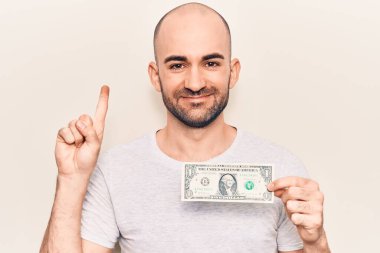 Genç yakışıklı kel adam elinde bir dolar banknotla gülümsüyor bir fikir ya da soru işareti ile mutlu bir yüzle, bir numara 