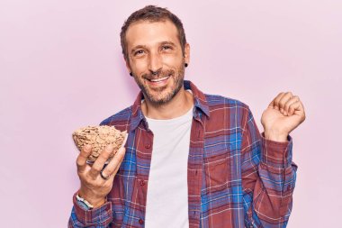 Genç yakışıklı adam mısır gevreği tutuyor gururla bağırıyor zaferi kutluyor ve başarıyı kollarını kaldırarak kutluyor. 