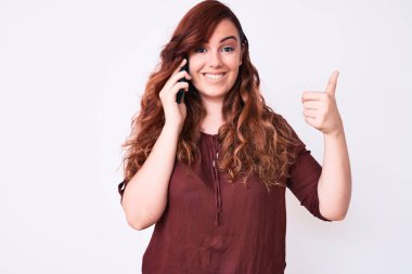 Genç ve güzel bir kadın akıllı telefonda konuşurken mutlu ve olumlu gülümsüyor, başparmağıyla mükemmel ve onay işareti yapıyor. 