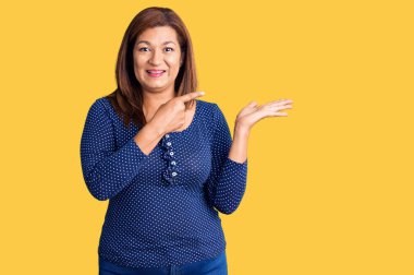 Orta yaşlı Latin kadın gündelik giysiler giyip kameraya hayret ediyor ve gülümsüyor.. 