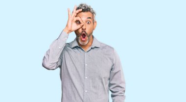 Orta yaşlı, gri saçlı, sıradan kıyafetler giyen, şaşırmış yüzüyle şaşırmış, parmaklarından bakan bir adam. İnançsız ifade. 