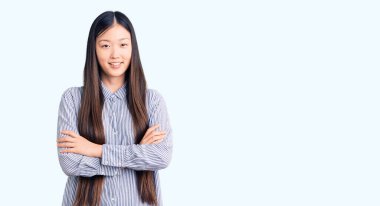 Kollarını kavuşturup kameraya bakarken gülümseyen gündelik tişört giyen genç, güzel Çinli bir kadın. pozitif kişi. 