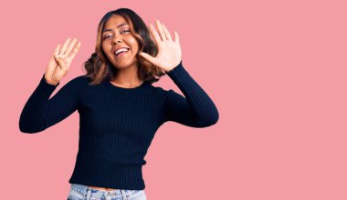 Genç, güzel, melez, günlük kıyafetler giyen, dokuz numaralı parmaklarını göstererek gülümseyen, kendinden emin ve mutlu bir kadın.. 