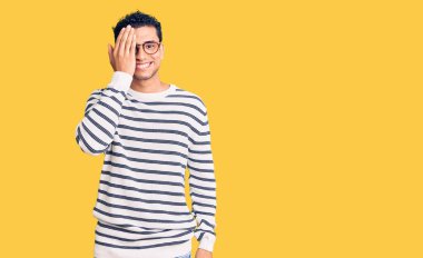 İspanyol asıllı yakışıklı genç adam gündelik kıyafetler giyiyor ve gözlük takıyor bir gözünü eliyle kapatıyor, yüzünde kendine güvenen bir gülümseme ve şaşırtıcı bir duygu var.. 