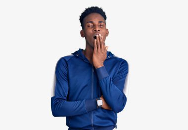 Genç Afro-Amerikan erkek spor giysisi giymekten sıkılmış. Ağzı eliyle kapatmaktan sıkılmış. Huzursuz ve uykulu.. 