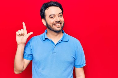 Bir fikir veya soruyla gülümseyen gündelik kıyafetler giyen genç İspanyol adam, bir numara, mutlu bir yüzle işaret ediyor. 
