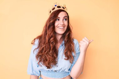 Prenses tacı takan genç ve güzel bir kadın başparmağını yana doğru uzatıyor ve ağzı açık gülümsüyor. 