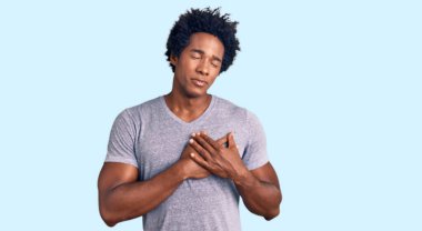 Yakışıklı Afro saçlı, sıradan kıyafetler giyen, göğsünde elleri kapalı, yüzünde minnet dolu bir jest olan Afro-Amerikan erkeği. sağlık kavramı. 