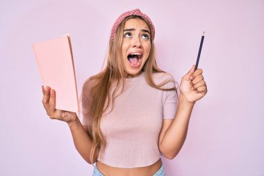 Genç, sarışın bir kadın elinde kitap ve kalemle kızgın ve kızgın bağırıyor sinirlenmiş ve öfkeli, öfkeyle bağırıyor.. 