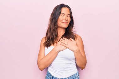 Beyaz arka planda kolsuz tişört giyen, elleri göğsünde gülümseyen güzel esmer bir kadın. Yüzünde minnet dolu bir jest ile gözleri kapalı. Sağlık kavramı.