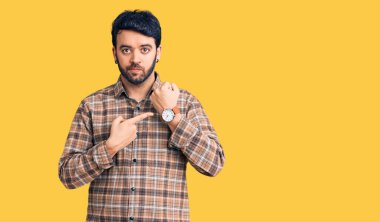 Gündelik kıyafetler giyen genç İspanyol adam saati, sabırsızlığı ve rahat bir ifadeyle kameraya bakmayı işaret ediyor. 