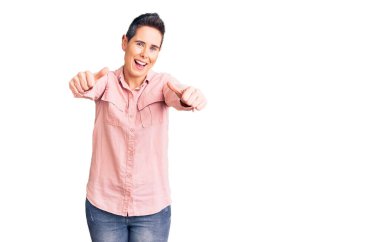 Kısa saçlı, günlük giysiler giyen, el hareketleriyle olumlu jest yapan, gülümseyen ve başarı için sevinen genç bir kadın. kazanan jest. 