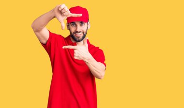 Sakallı, teslimat üniforması giyen, gülümseyen, elleri ve parmakları gülen yüzlü genç yakışıklı bir adam. yaratıcılık ve fotoğrafçılık kavramı. 