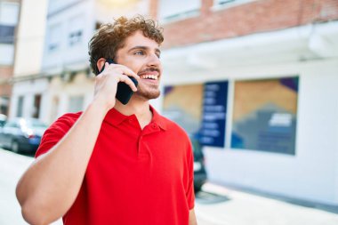 Genç yakışıklı beyaz adam mutlu gülümsüyor. Şehirdeki akıllı telefondan konuşuyorlar..