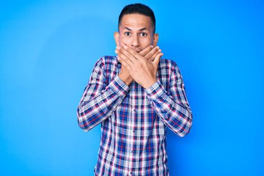 Gündelik kıyafetler giyen genç, yakışıklı Latin adam yanlışlıkla elleri ile ağzını kapatırken şok oldu. gizli kavram. 