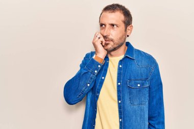 Günlük kıyafetler giyen genç yakışıklı adam gergin ve gergin görünüyor. Ağzı tırnak yiyen eller. anksiyete. 