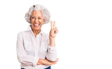 Gri saçlı, sıradan kıyafetler giyen, kameraya gülümseyen ve zafer işareti yapan yaşlı bir kadın. İki numara.. 