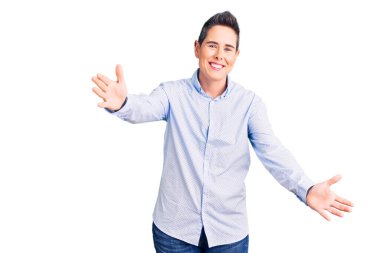 Kısa saçlı genç bir kadın iş kıyafetleri içinde kameraya bakıyor ve sarılmak için kollarını açmış gülümsüyor. Mutluluğu kucaklayan neşeli bir ifade.. 