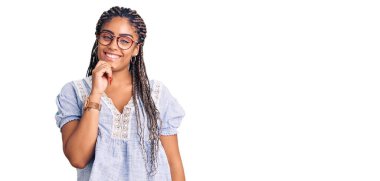 Saçları günlük kıyafetlerle, gözlükleriyle kameraya kendinden emin bir şekilde bakan kolları çapraz ve çenesi açık genç Afro-Amerikalı bir kadın. Olumlu düşünmek. 