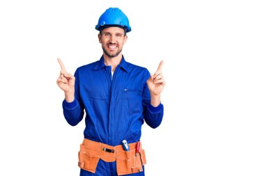 İşçi üniforması giyen ve kasketli gülümseyen, kendine güvenen, farklı yönleri gösteren genç yakışıklı bir adam. reklam için kopyalama alanı 