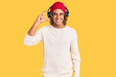 Genç İspanyol adam müzik dinliyor kulaklık takıyor gülümsüyor ve el hareketleriyle hareket ediyor parmaklarıyla işaret yapıyor ve kameraya bakıyor. ölçüm kavramı. 