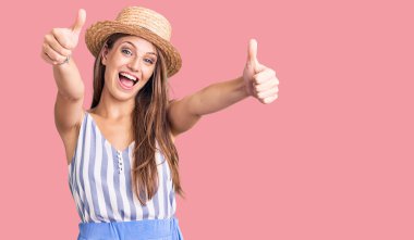 Sarışın, yaz şapkası takan genç ve güzel bir kadın. Elleriyle olumlu bir jest yapıyor. Gülümsüyor ve başarı için seviniyor. kazanan jest. 