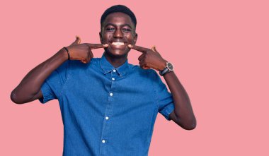 Gündelik kıyafetler giyen, neşeli gülümseyen, parmaklarıyla ve ağzıyla işaret eden Afrikalı genç bir Amerikalı. diş sağlığı kavramı. 