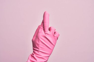 İzole edilmiş pembe arka plan üzerinde temizleme eldiveni olan beyaz bir gencin eli. Parmakları çapraz, batıl inançlar ve şanslı bir jest, şanslı ve umut ifadesi.