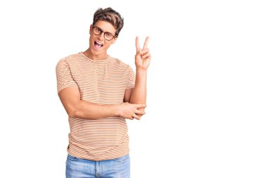 Gündelik kıyafetler ve gözlük takan genç yakışıklı adam kameraya bakıp gülümsüyor ve zafer işareti yapıyor. İki numara.. 