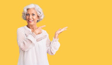 Kıdemli gri saçlı kadın, sıradan kıyafetler giyip kameraya hayret ediyor ve gülümsüyor.. 