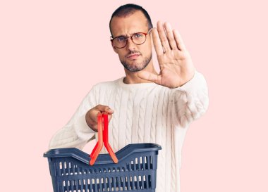 Elinde süpermarket sepeti olan yakışıklı bir adam dur işareti yapıyor ciddi ve kendinden emin bir ifadeyle, savunma jesti yapıyor. 