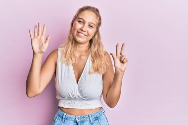 Gündelik kıyafetler giyen genç sarışın kız sekiz numarayı gösterip işaret ederken kendinden emin ve mutlu gülümsüyor.. 