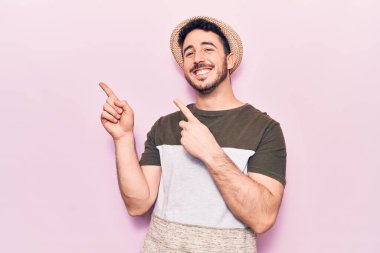 Gündelik kıyafetler giyen genç İspanyol adam gülümseyip kameraya bakıyor ve iki eliyle ve parmaklarıyla kenarı işaret ediyor.. 