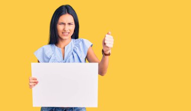 Boş pankart tutan genç ve güzel Latin kız öfkeyle bağırıyor, öfkeyle bağırıyor ve el kaldırıyor. 