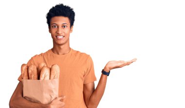 Afrika kökenli Amerikalı genç bir adam elinde kağıt torbayla gülümseyen, mutlu bir şekilde sunan ve avuç içi kameraya bakan bir adam.. 