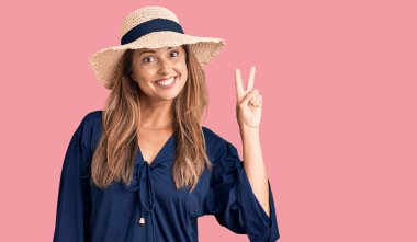Orta yaşlı İspanyol kadın yaz şapkası takıyor ve parmaklarını iki numara ile göstererek gülümsüyor.. 