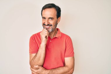 Orta yaşlı İspanyol bir adam gündelik kıyafetler giyip kameraya bakıyor kollarını kavuşturup gülümseyerek ve çenesini kaldırarak. Olumlu düşünmek. 