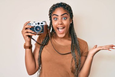 Örgülü, klasik fotoğraf makinesi olan genç Afrikalı Amerikalı kadın zaferi mutlu bir gülümseme ve ellerini kaldırarak kazanan ifadeyle kutluyor. 