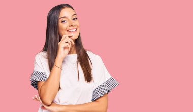 Günlük kıyafetler giyen genç İspanyol kadın kameraya kendinden emin bakıyor kollarını kavuşturup gülümseyerek ve çenesini kaldırarak. Olumlu düşünmek. 