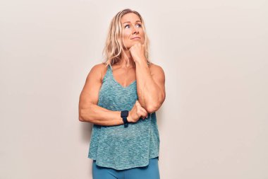 Orta yaşlı, beyaz kadın spor giyer, çenesi çenesine dayanmış soru sorar, düşünceli bir ifade takınır. Düşünceli bir yüzle gülümsüyor. şüphe kavramı. 